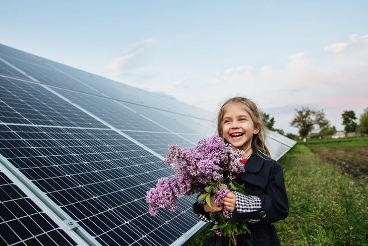 A child with a future of alternative energy and sustainable energy. The child holds flowers on a background of solar panels, photovoltaic. Environmental friendliness and clean energy concept.